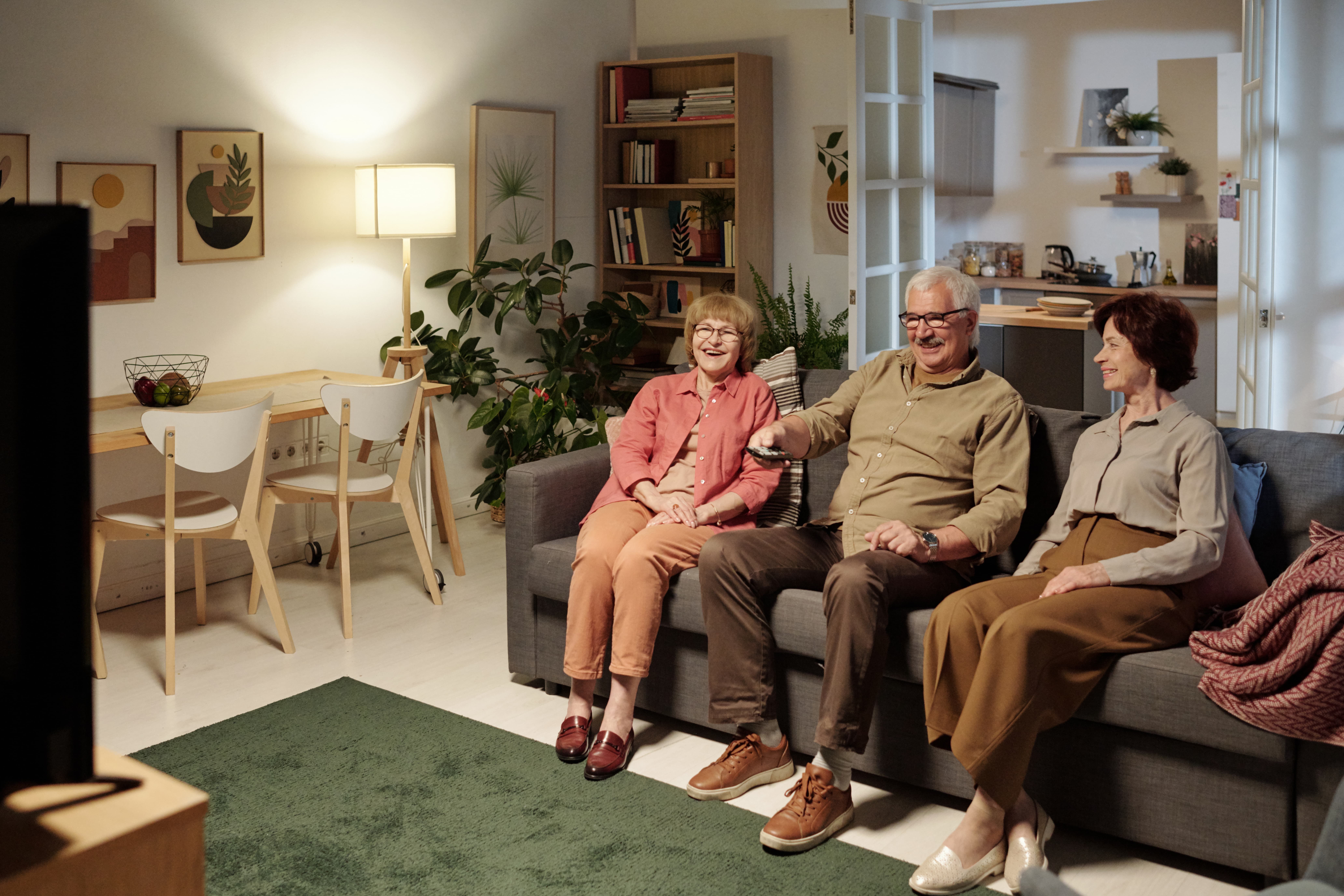 three aged friends casualwear sitting sofa while man choosing tv channel  1 